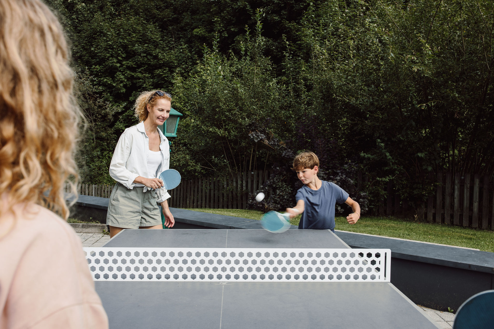 Erwachsene und Kind spielen draußen Tischtennis