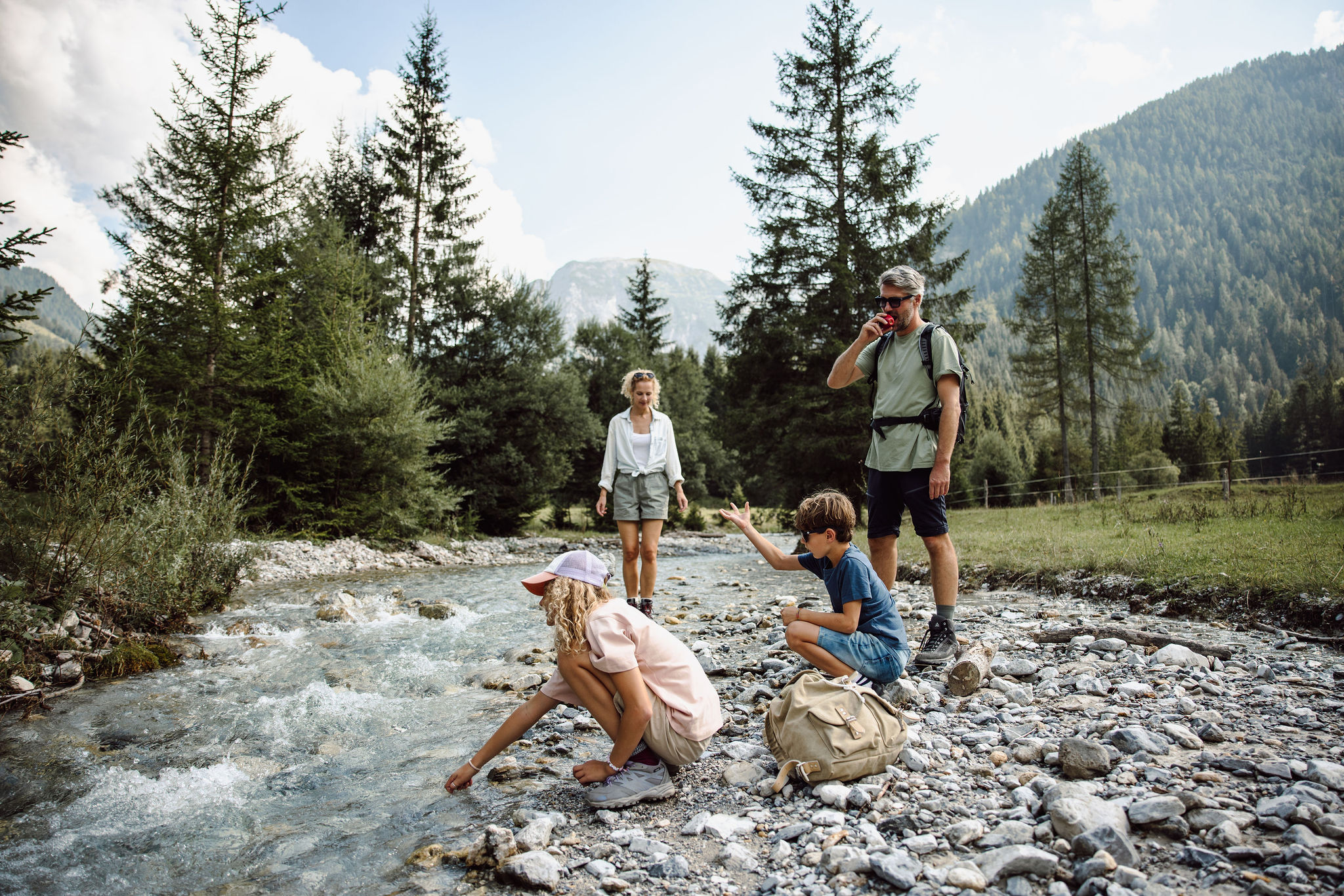 Familie wandert am Fluss in den Bergen, zwei Kinder spielen am Ufer